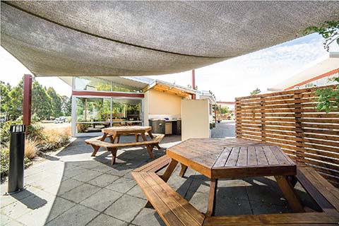 Two wooden hexagonal picnic tables located in an outdoor area with a shade sail over top