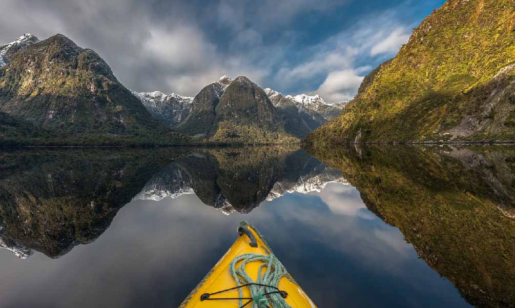 Looking over the front tip of a yellow kayak towards the majestic mountains and waters of Doubtful Sound
